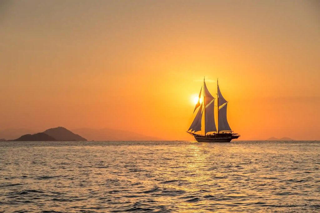A phinisi silhouetted under sail against a Komodo sunset