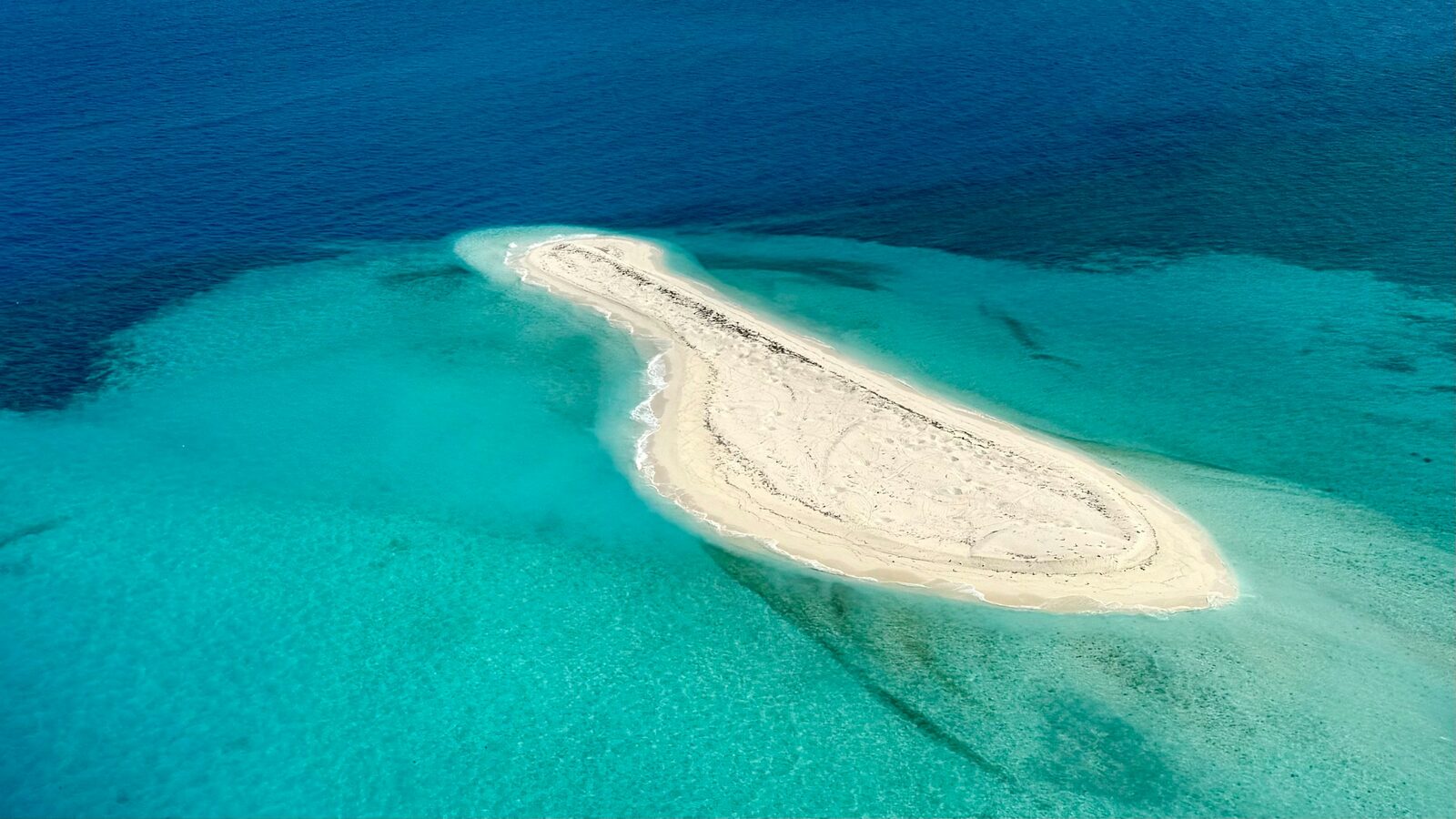 Aerial view of a narrow sandbar surrounded by clear turquoise shallows