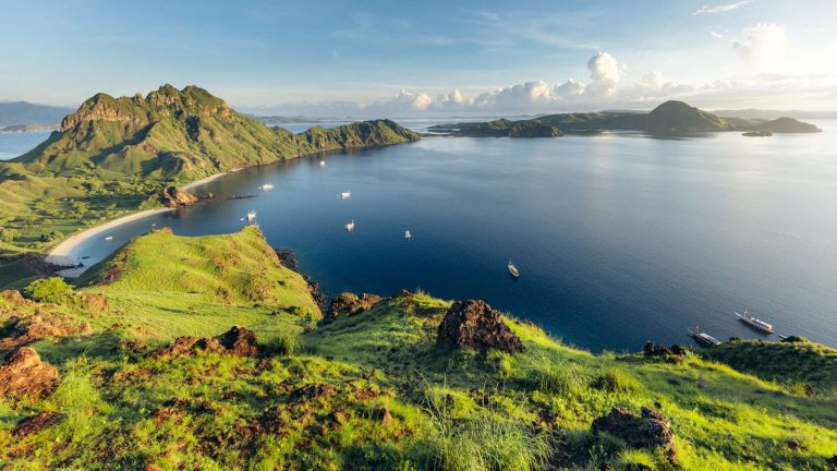 Boats anchored in a sheltered bay in Komodo National Park photographed from a grassy hilltop viewpoint