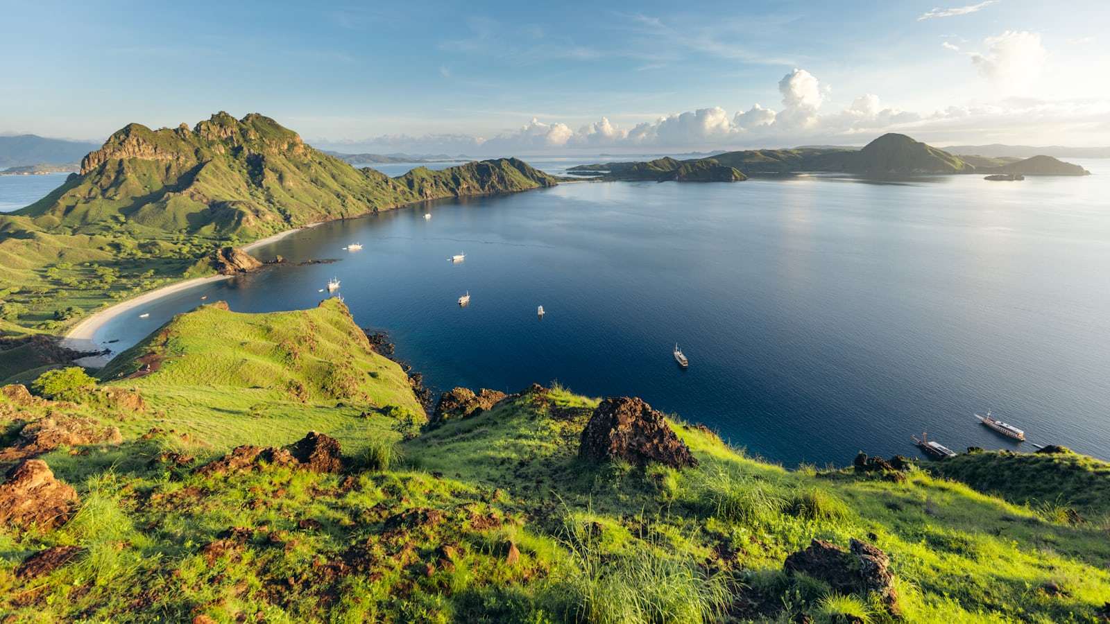 Boats anchored in a sheltered bay in Komodo National Park photographed from a grassy hilltop viewpoint