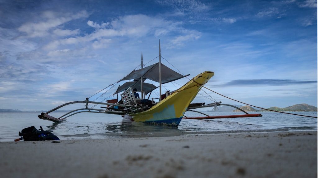 A traditional outrigger boat rests on a sandy beach