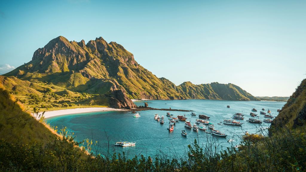 Boats at anchor in a calm, sheltered bay below the hills of Padar Island, Komodo National Park