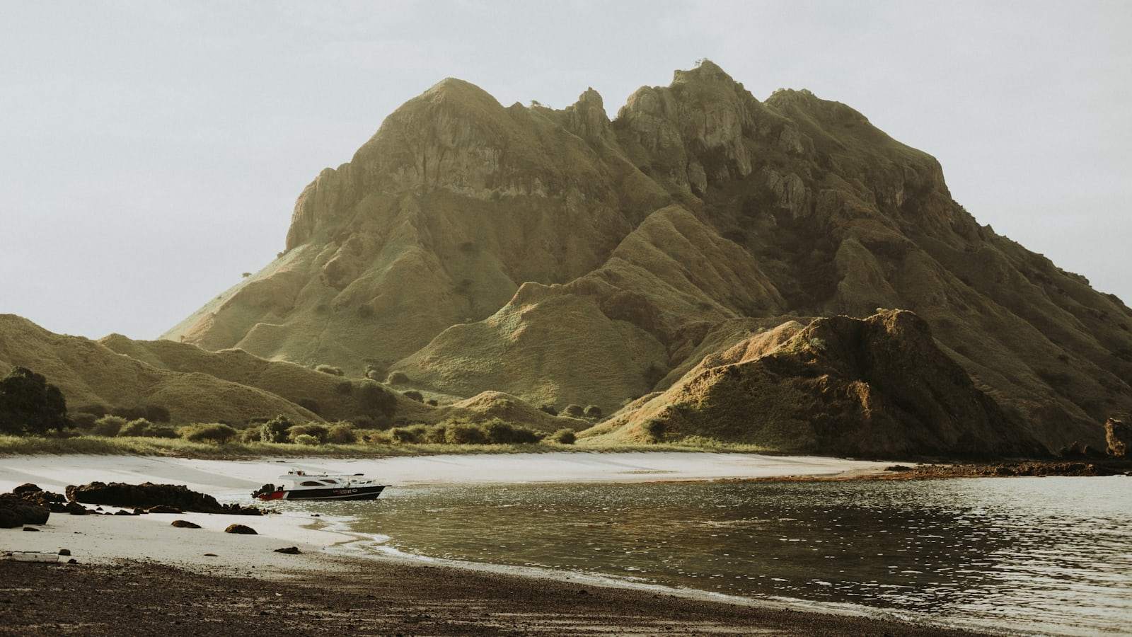 Person riding on white boat on sea near brown mountain during daytime