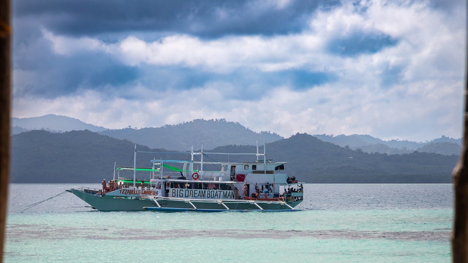 A boat floats on turquoise water near misty mountains