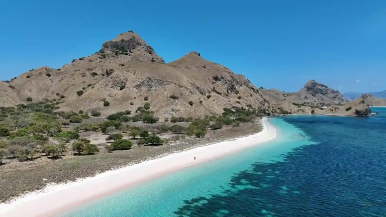 The pink sand of Pink Beach curving into clear water