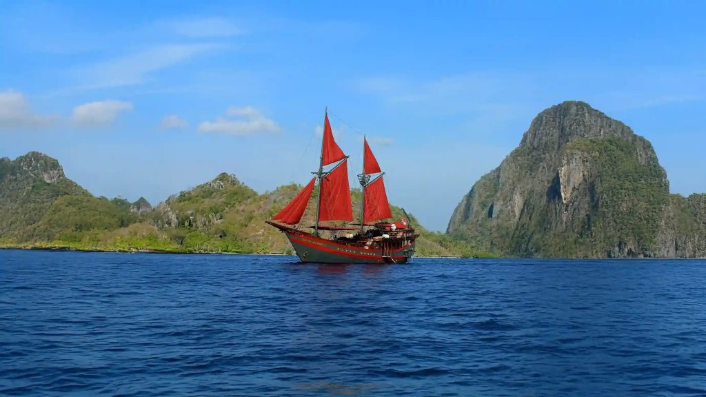 A traditional phinisi with red sails under way