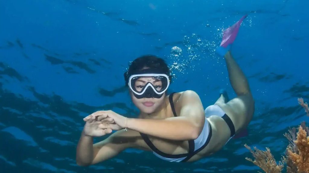 A freediver moving over the reef with a camera